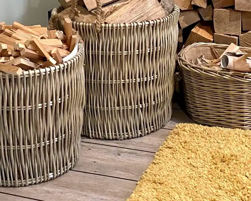 Two tall willow log baskets filled with logs beside a hearth